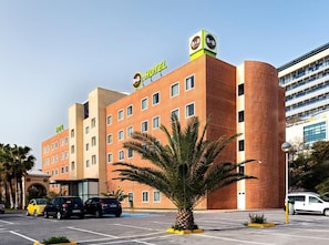 A hotel with a modern brick facade, multiple balconies, and a parking lot with several cars.