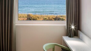 Ein Zimmer mit Fenster und Meerblick, ein Sessel und ein Schreibtisch mit Lampe.
