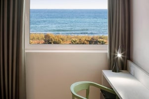 Une pièce avec une fenêtre donnant sur la mer, une chaise et un bureau avec une lampe.