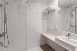 A modern bathroom with a glass shower enclosure, a white sink, and a towel rack.