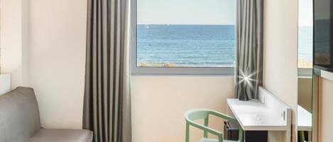 A hotel room with a bed, a desk, a chair, a TV, and a view of the sea.