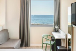 Une chambre d’hôtel avec un lit, un bureau, une chaise, une télévision et une vue sur la mer.