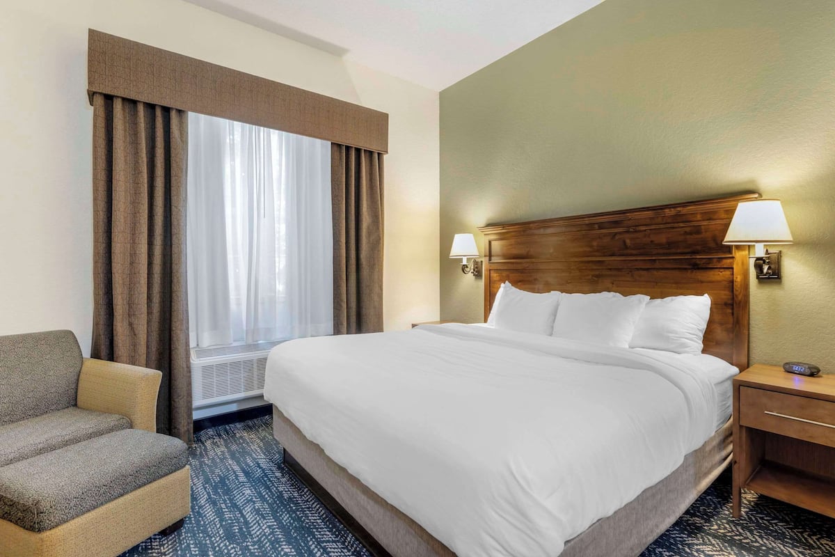 A hotel room with a large bed, a chair, a nightstand, and a window with curtains.
