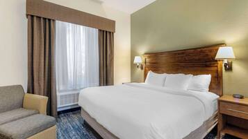 Ein Hotelzimmer mit einem großen Bett, einem Sessel, einem Nachttisch und einem Fenster mit Vorhängen.
