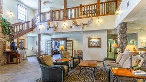 A spacious lobby with a high ceiling, a staircase, leather sofas, a patterned rug, and a stone pillar. - Comfort Inn & Suites Mt. Rushmore (Keystone)