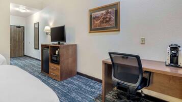 A hotel room with a bed, a desk with a computer, a television, a coffee maker, and a framed picture on the wall.