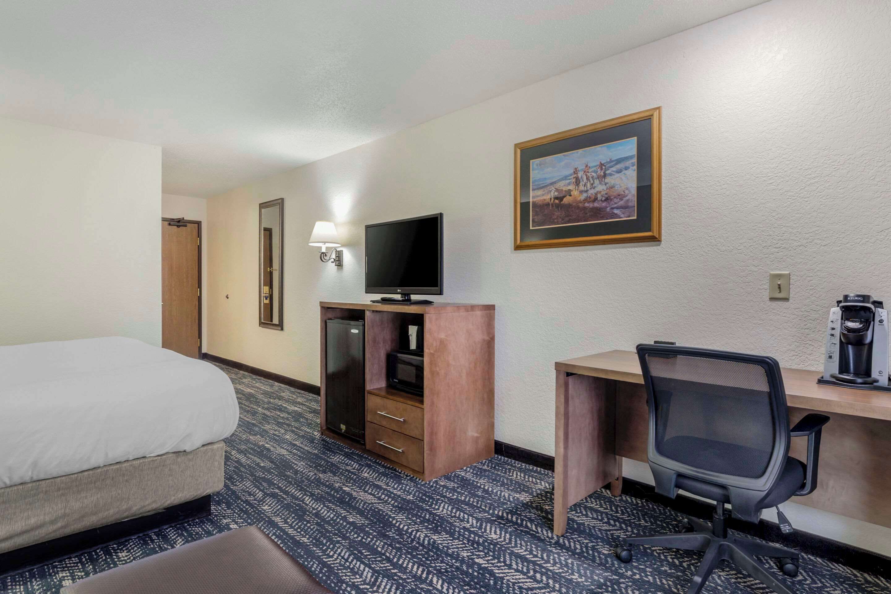 A hotel room with a bed, a desk with a computer, a TV, and a coffee maker.