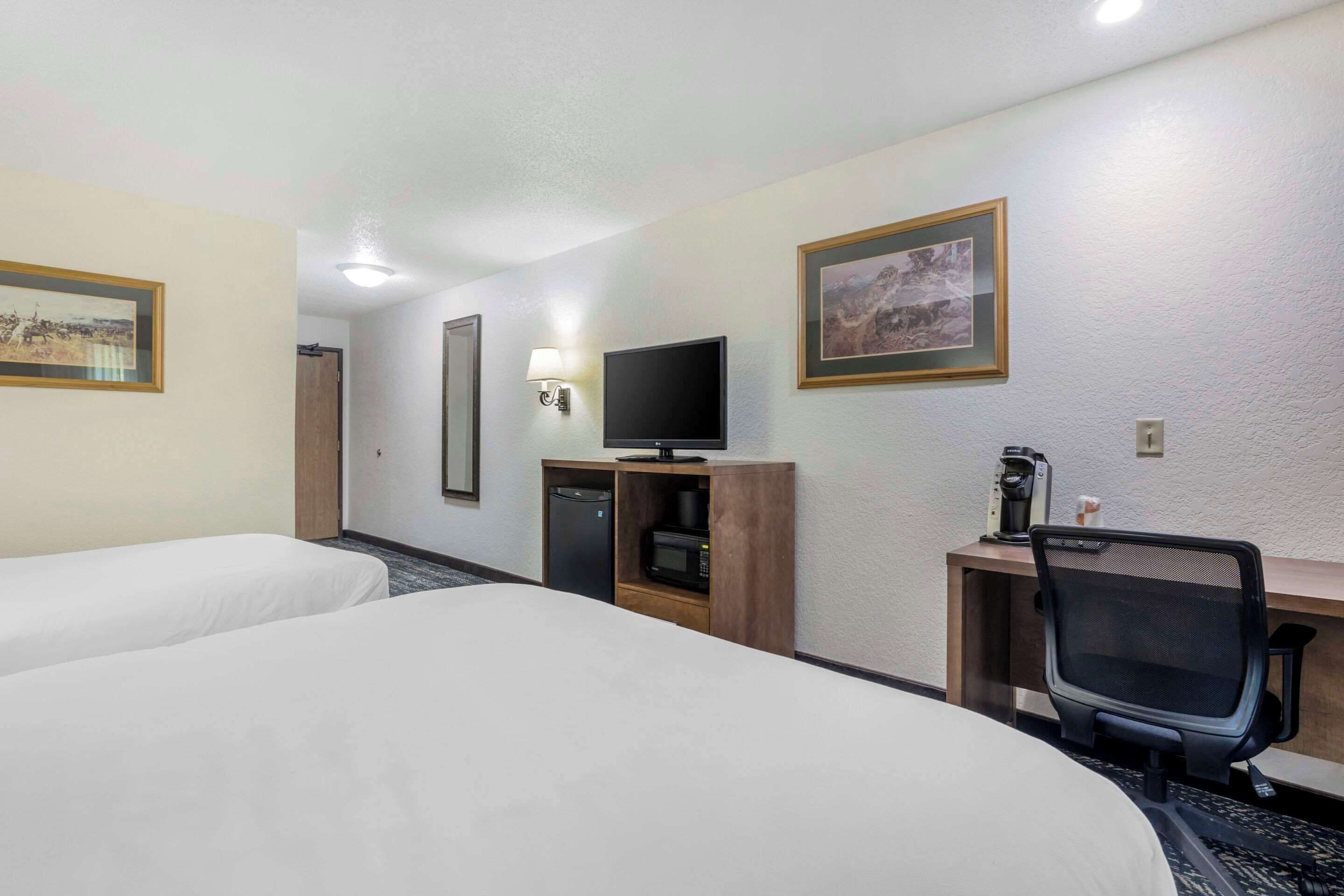 Habitación de hotel con dos camas, un escritorio con computadora, televisión y cafetera.
