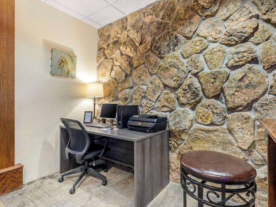 A home office with a stone wall, a desk with two monitors, a printer, and a leather chair.