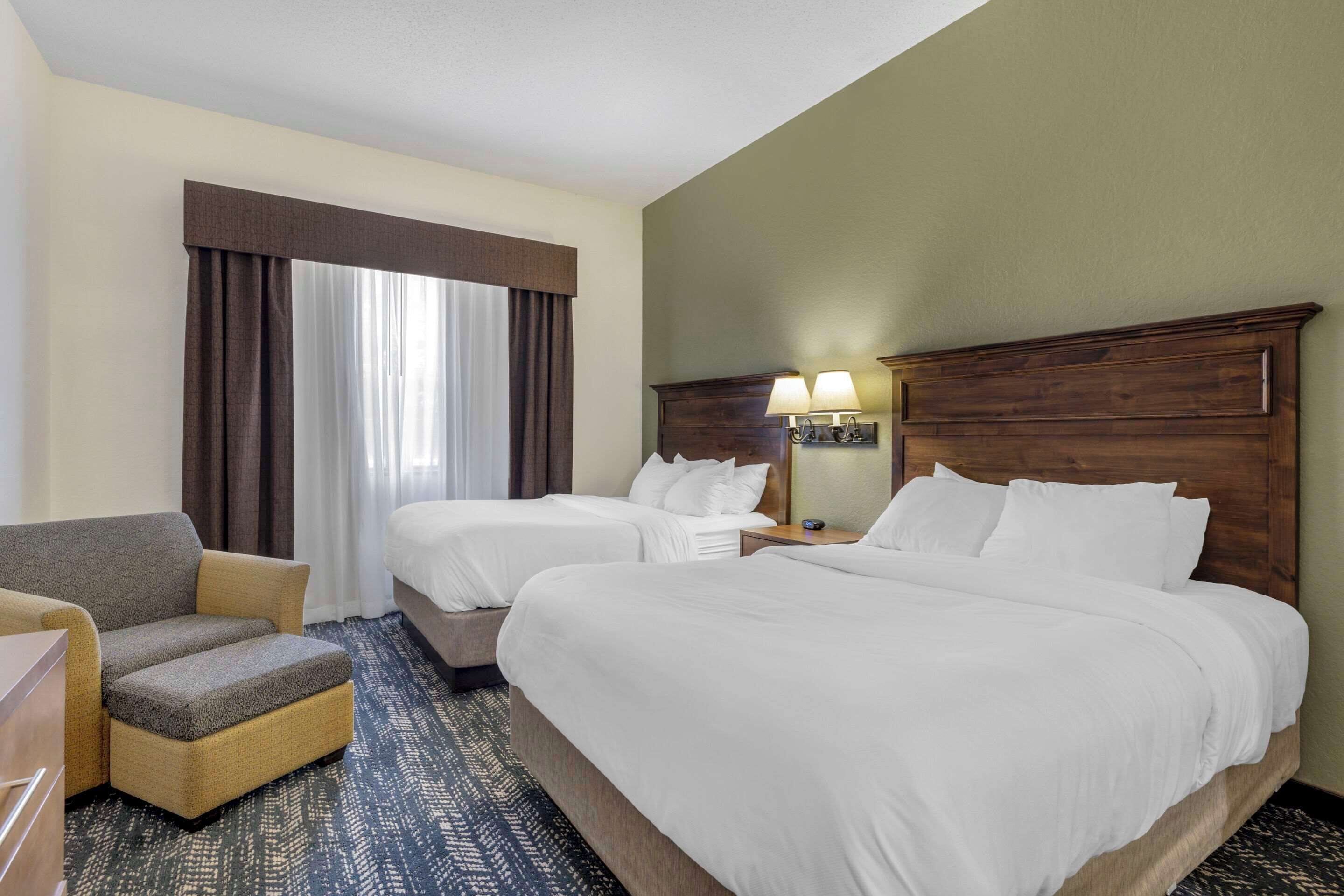 Habitación de hotel con dos camas, un sofá, una mesita de noche con lámparas y un ventanal con cortinas.