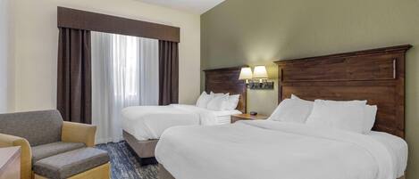 Habitación de hotel con dos camas, un sofá, una mesita de noche con lámparas y un ventanal con cortinas.