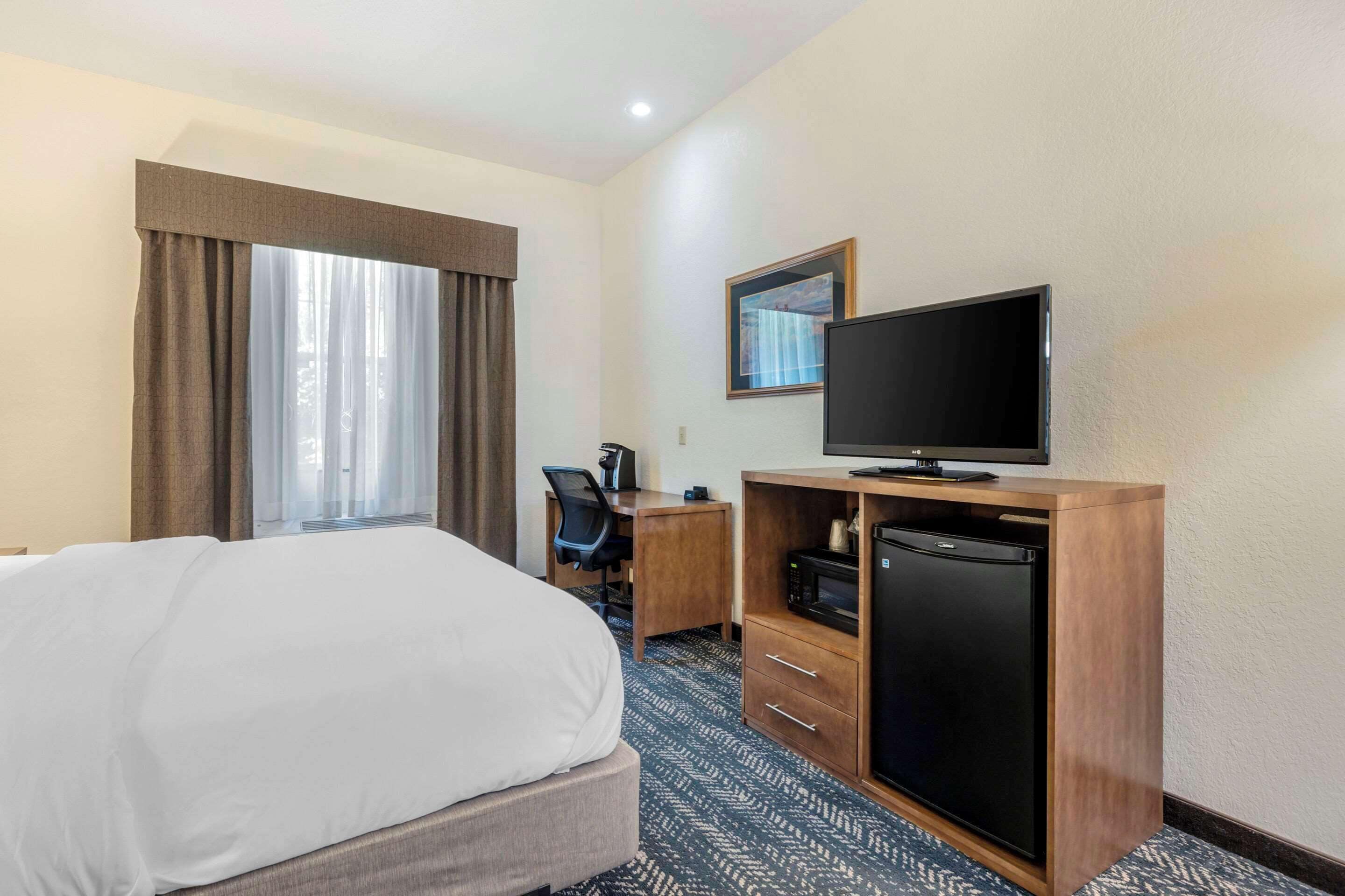 A hotel room with a bed, a desk with a chair, a television, and a refrigerator.