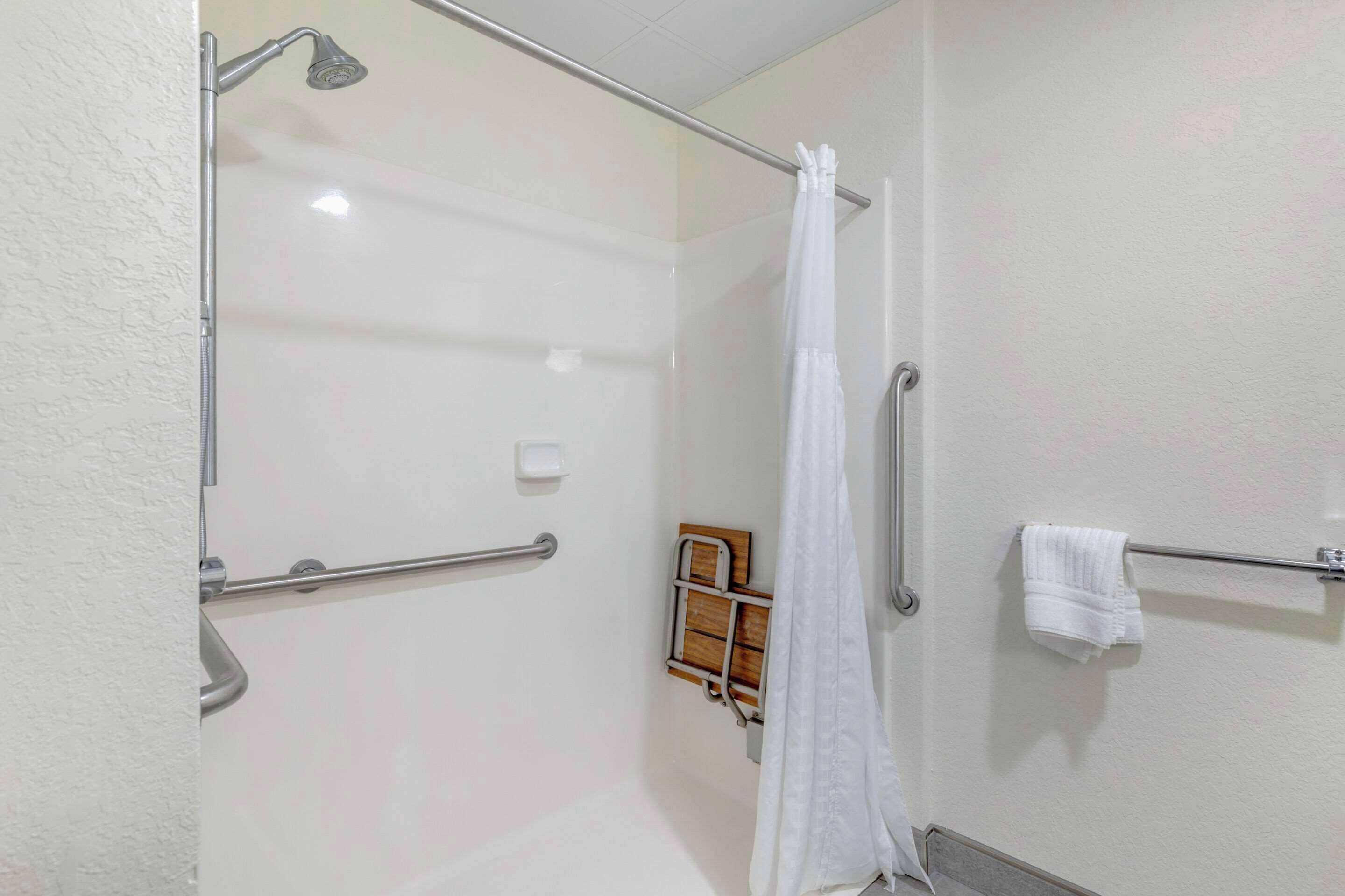 A shower area with a glass door, a white shower curtain, a grab bar, and a towel rack with a towel.