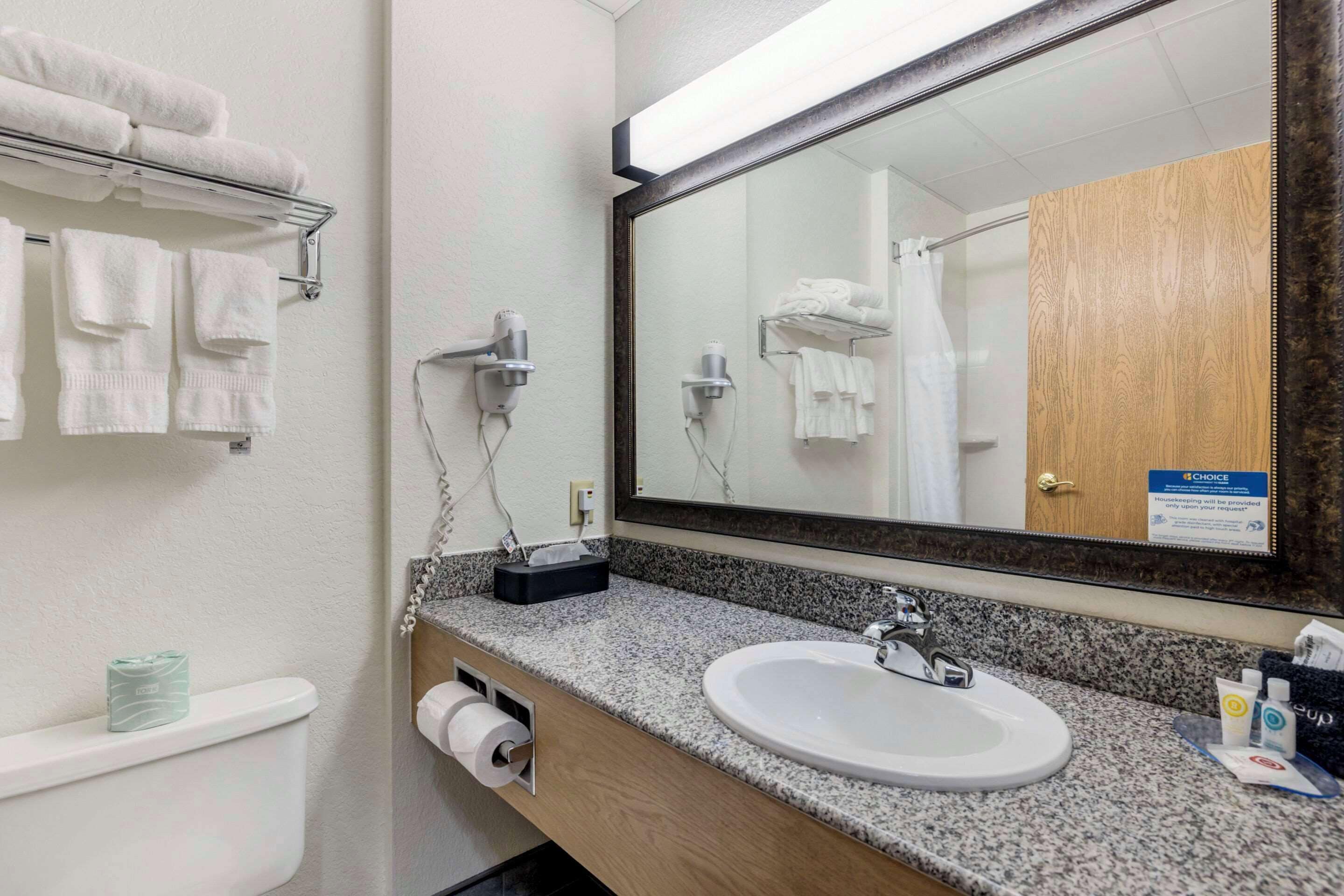 Un baño con lavamanos, espejo, toallero y dispensador de papel higiénico.