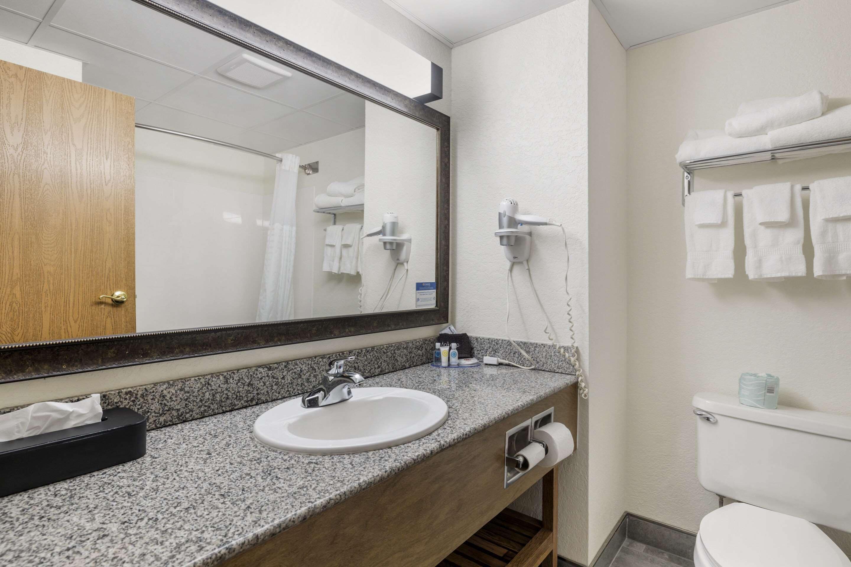 A bathroom with a granite countertop sink, a mirror, a towel rack, and a toilet.