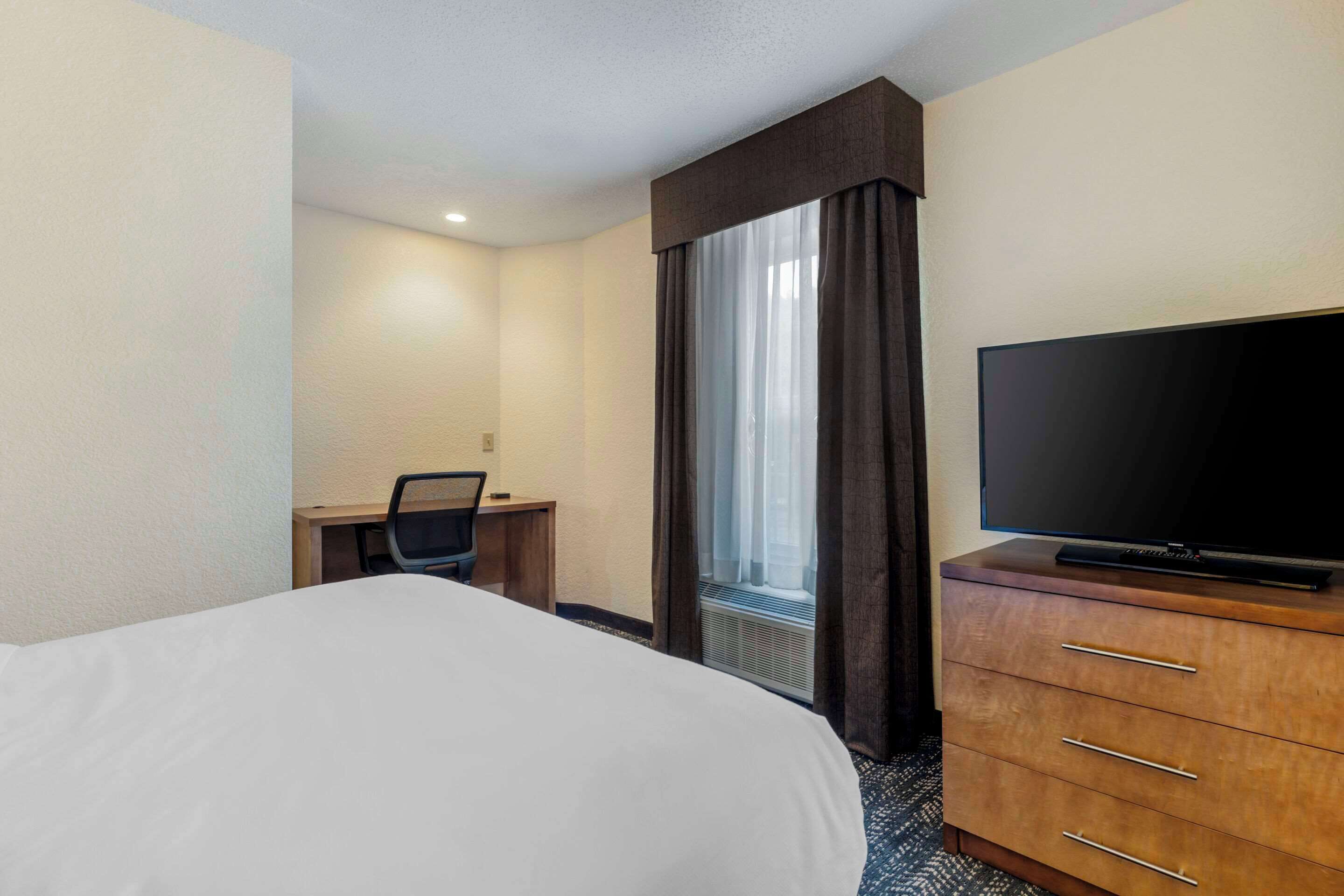 A hotel room with a bed, a desk, a television, and a window with curtains.