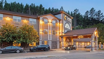 Un hotel Comfort Inn & Suites con entrada cubierta, varios coches estacionados al frente y árboles en el fondo.