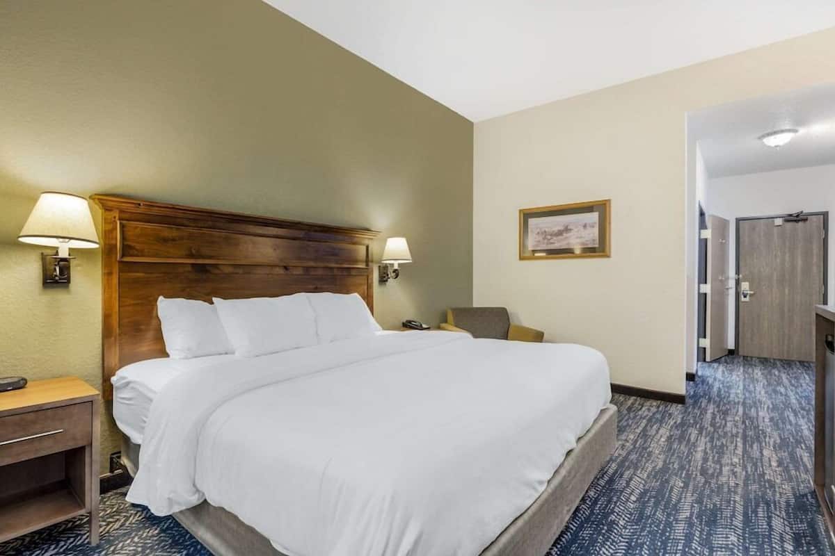 A hotel room with a large bed, bedside lamps, a chair, a desk, and a door.