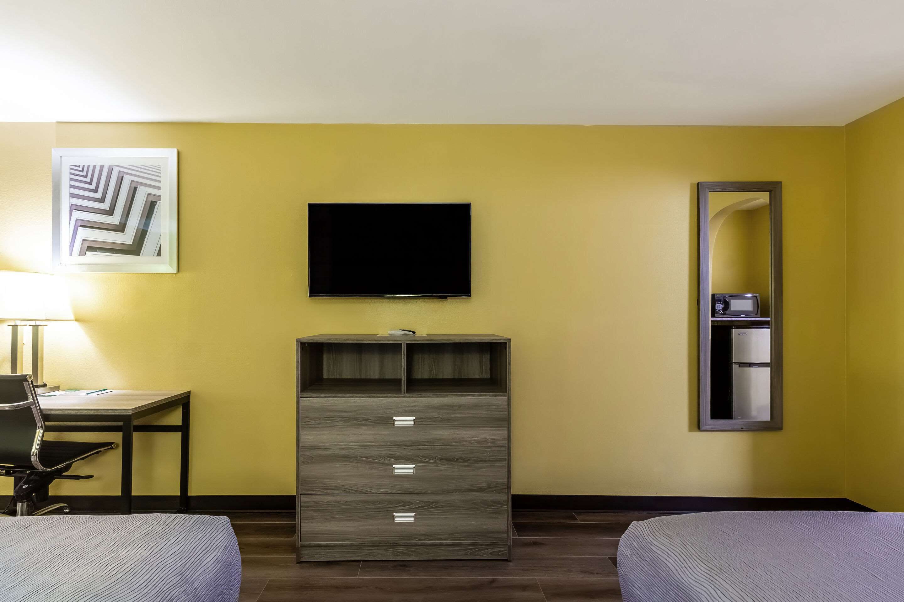 Une chambre d’hôtel avec deux lits, un bureau avec une chaise, une télévision, une armoire et un miroir.