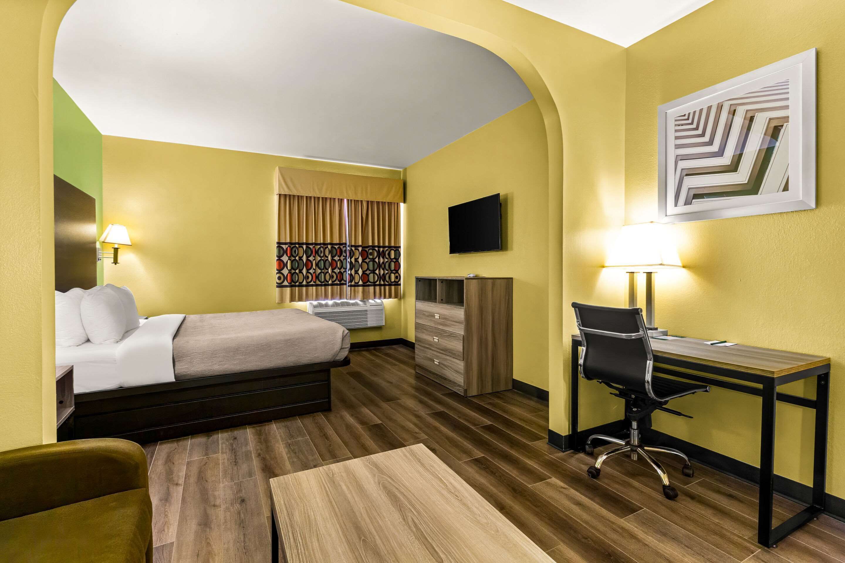 A hotel room with a bed, desk, chair, and a TV on the wall.