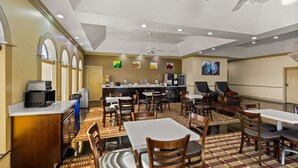 Comedor de hotel con mesas, sillas, una barra con una máquina de café y un ventilador de techo.