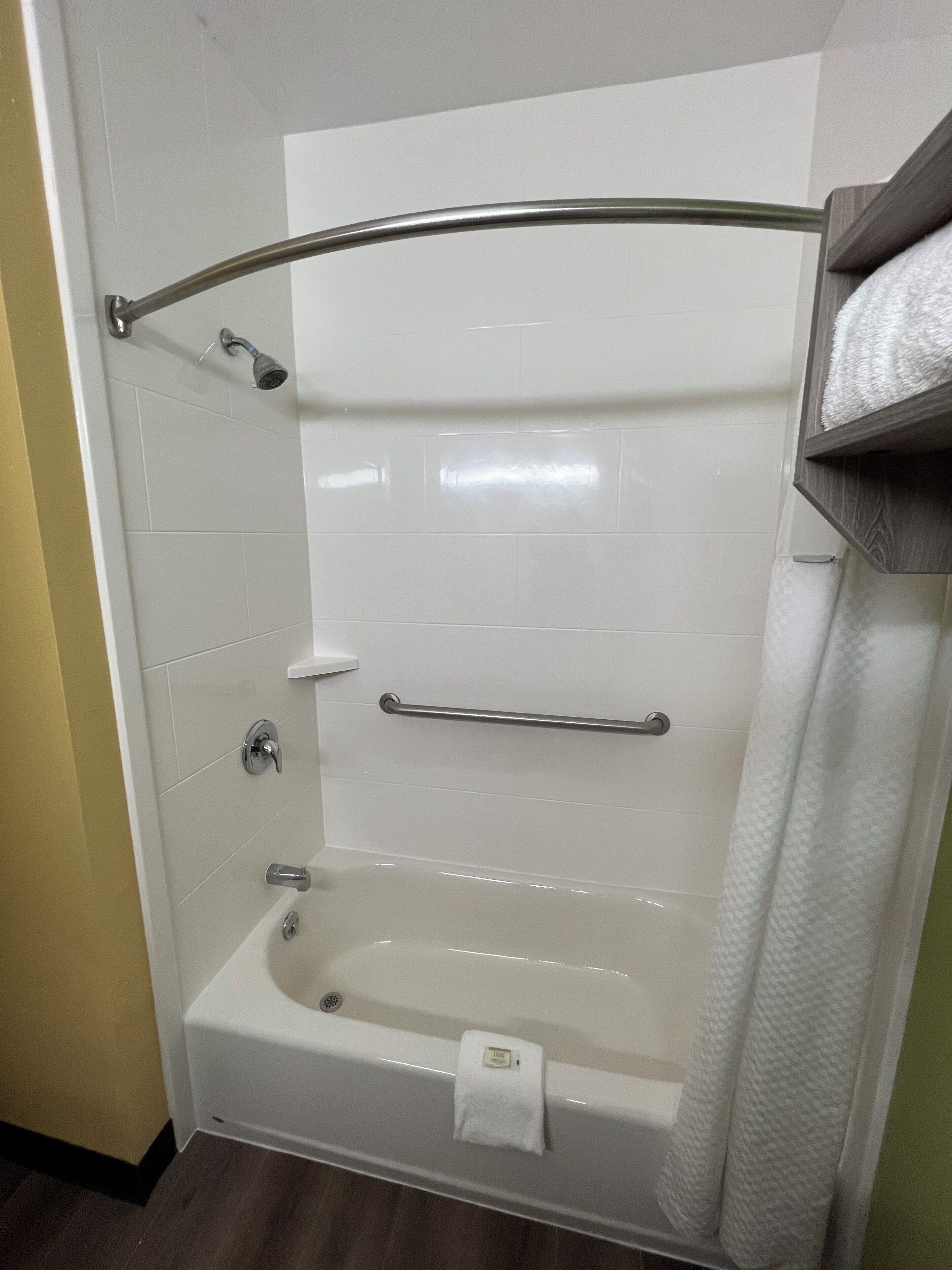Un baño moderno con bañera, ducha e inodoro. Hay un perchero y un estante con artículos de aseo.