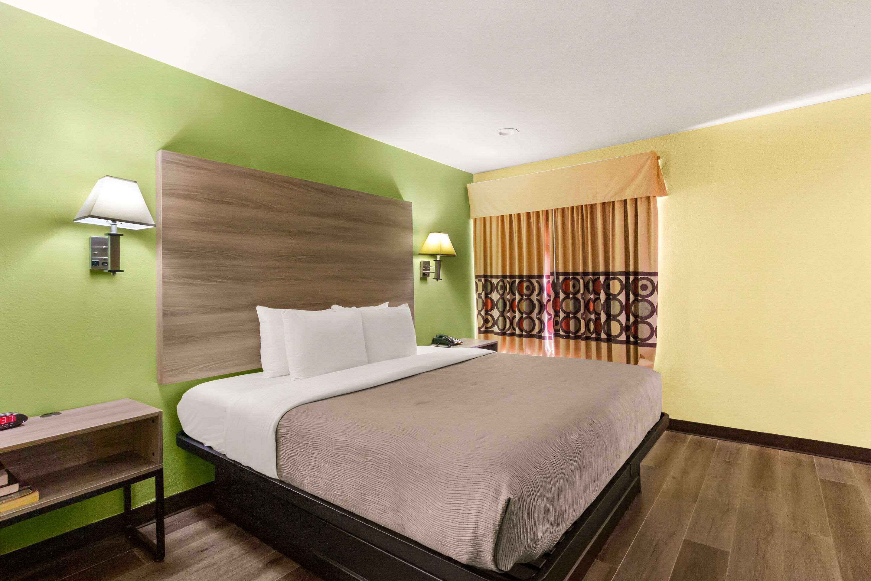 Une chambre d’hôtel avec un lit, des lampes de chevet, une table de chevet et un rideau à motifs.