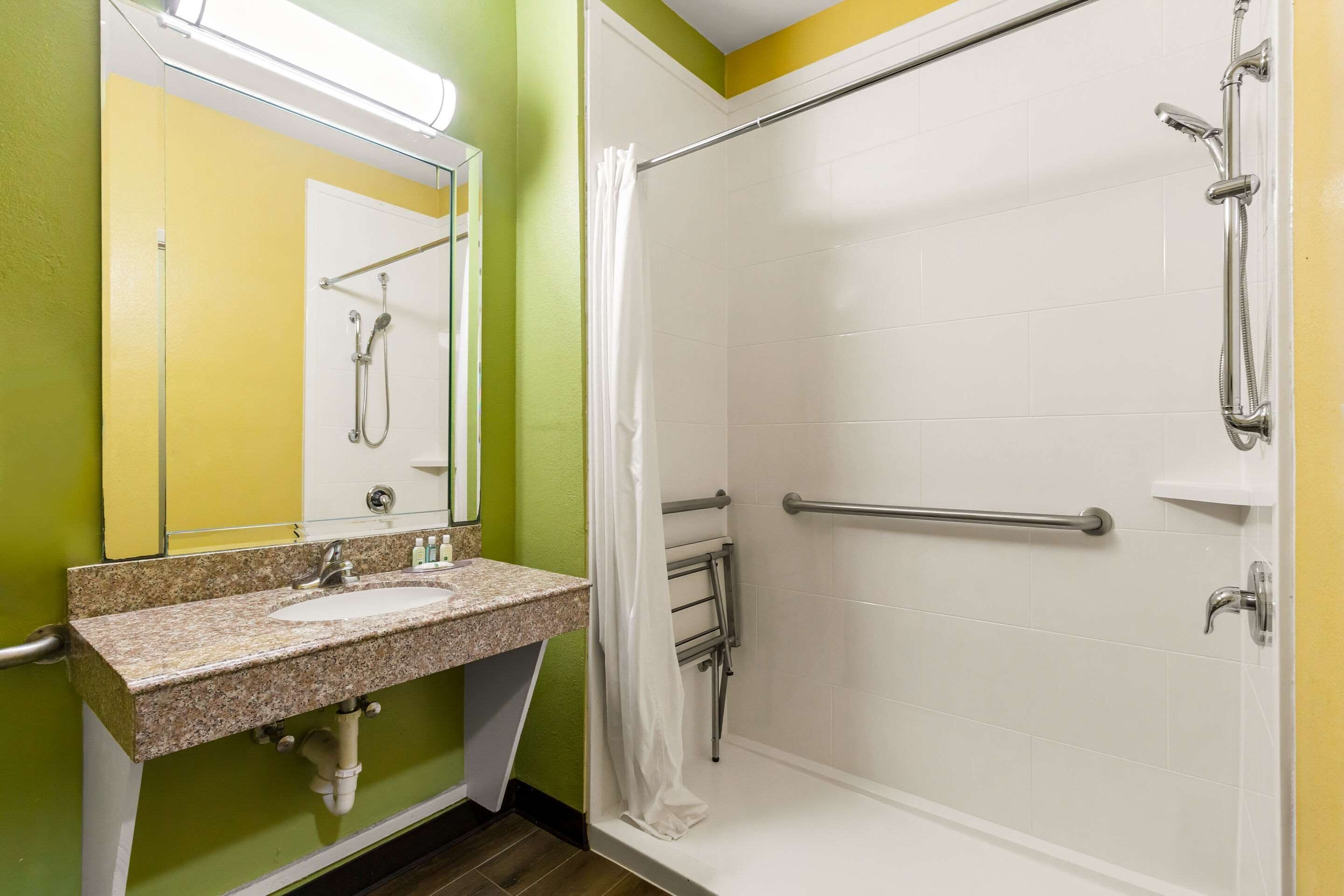 A bathroom with a sink, mirror, shower, and grab bars.