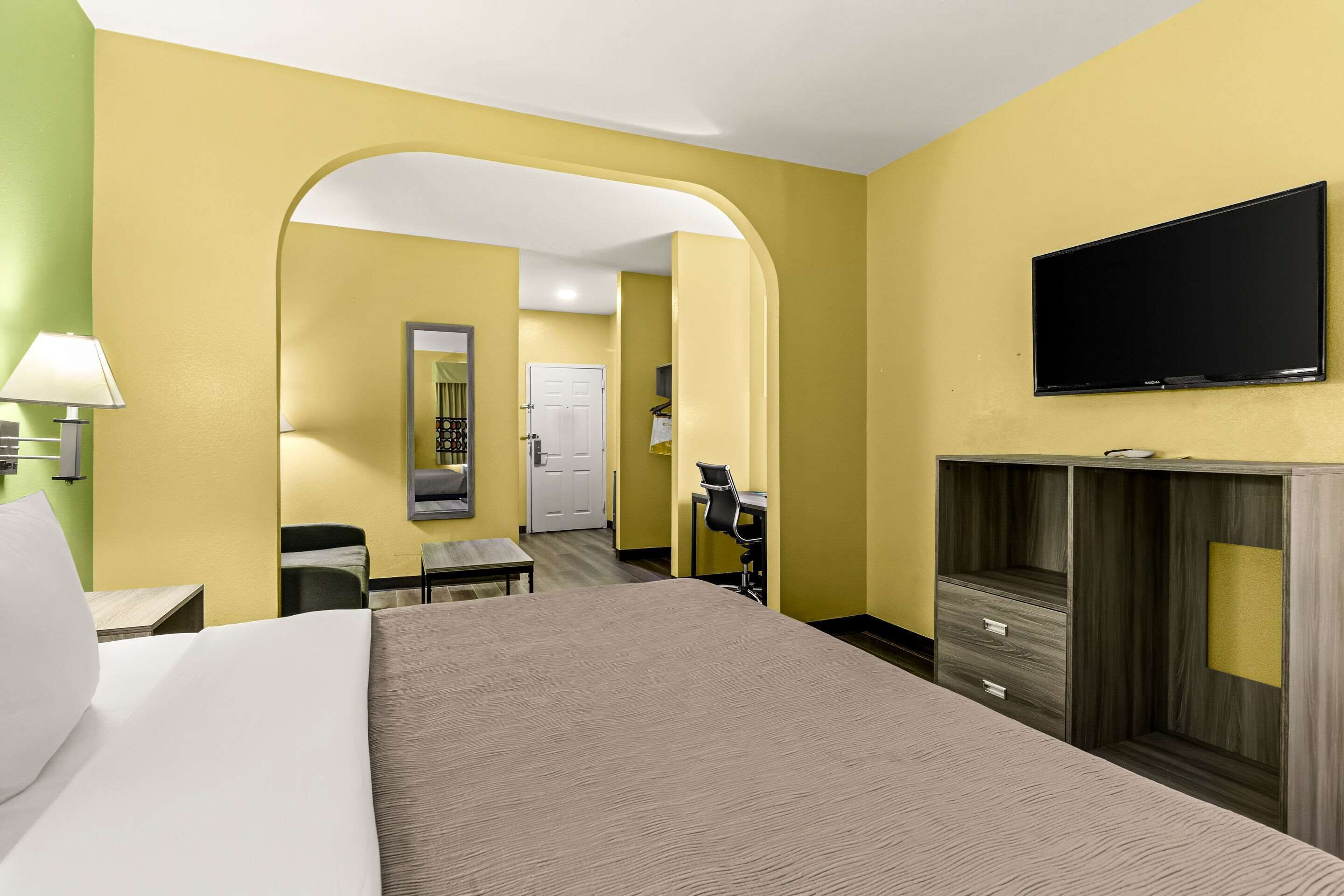 A hotel room with a bed, a desk, a chair, a TV, and a wardrobe.