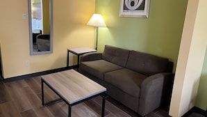 Una habitación pequeña y amoblada con un sofá, una mesa, una lámpara, un espejo y una obra de arte enmarcada en la pared.