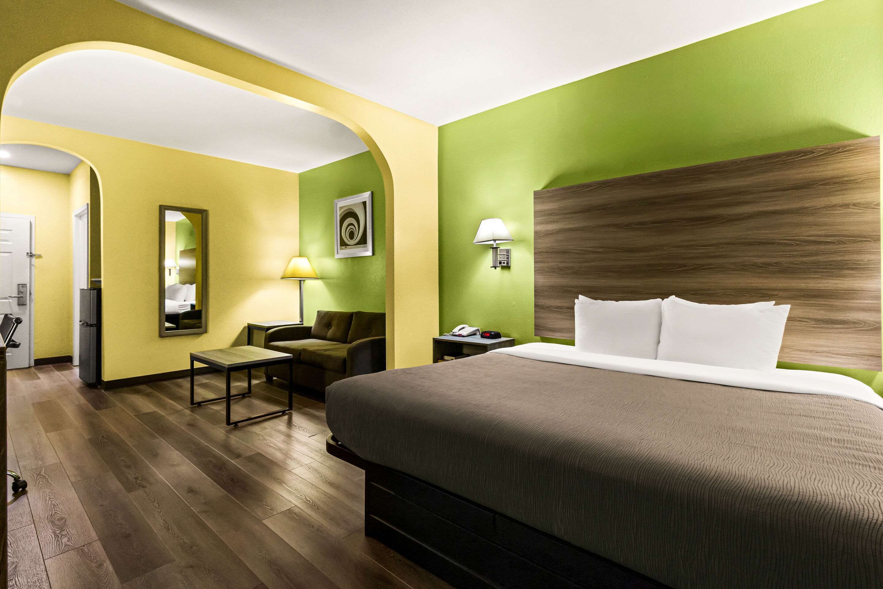 Quarto de hotel com uma cama grande, uma escrivaninha, uma cadeira, um abajur e uma mesinha.