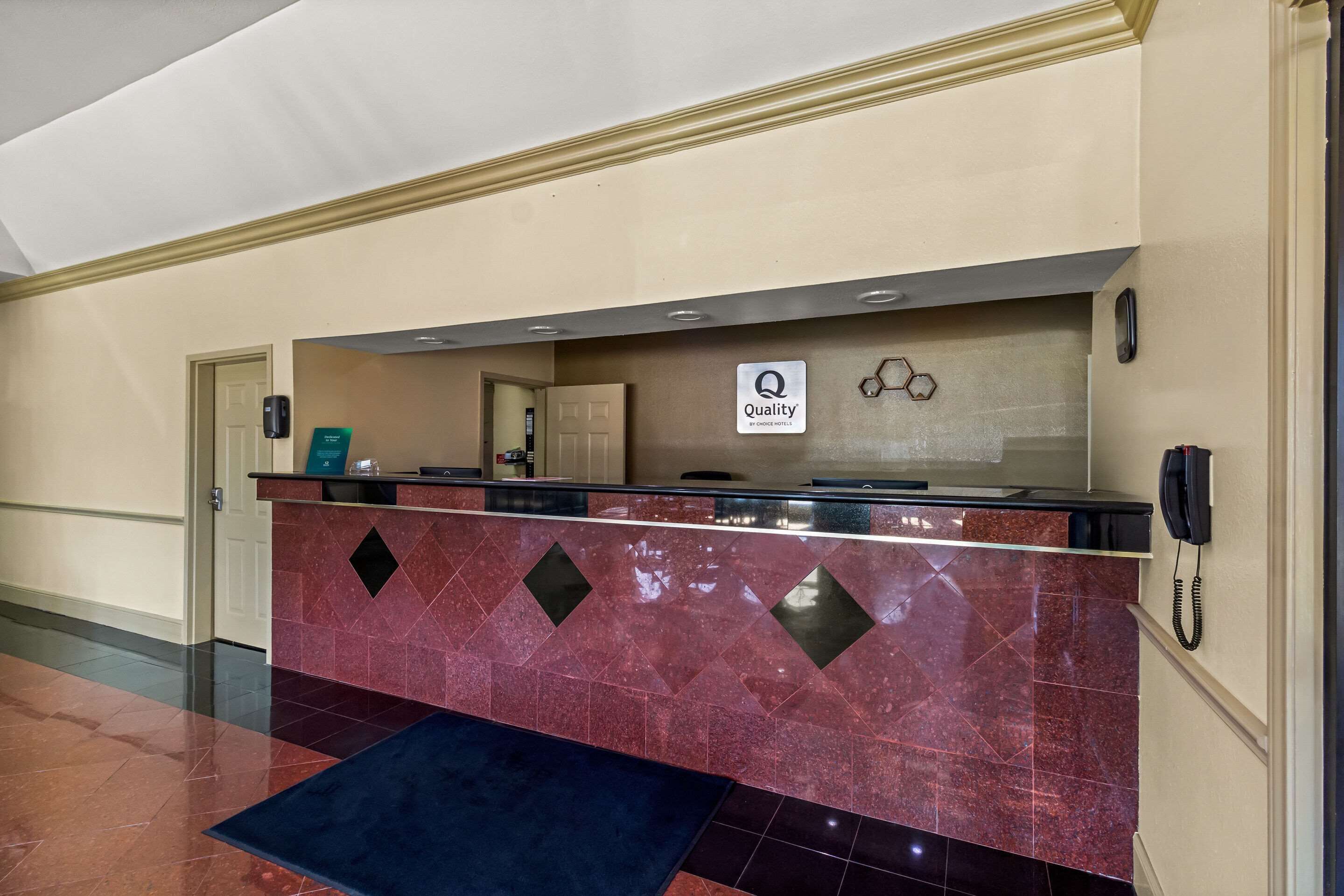 A hotel reception area with a marble counter, a sign indicating 'Quality by Chace Hotels', and a phone on the wall.