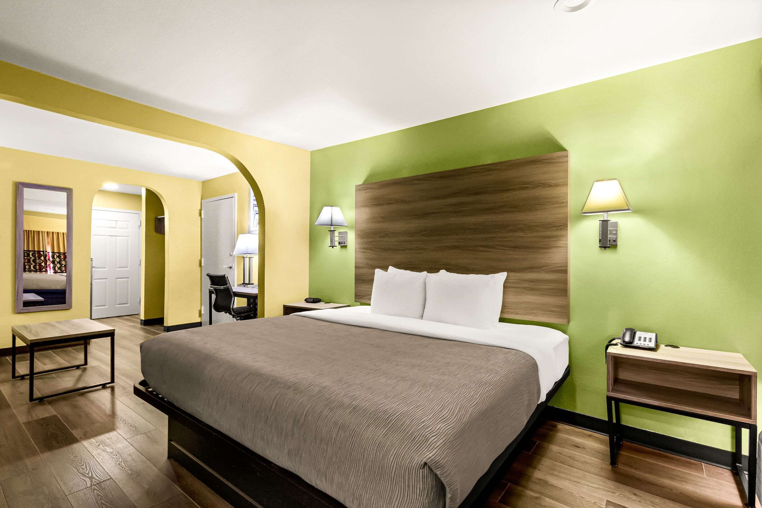 A hotel room with a large bed, bedside lamps, a nightstand, and a mirror.