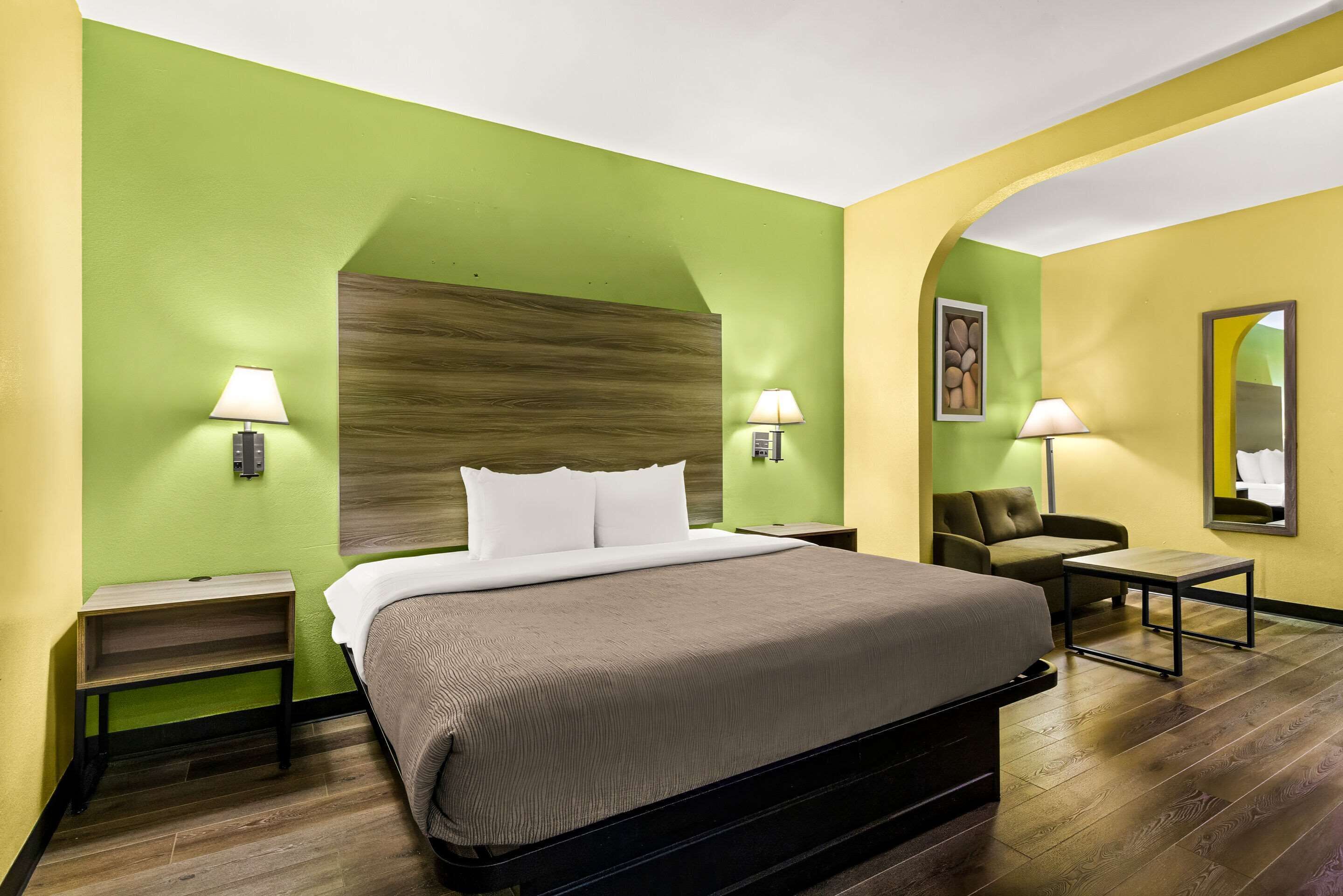 A hotel room with a large bed, two bedside tables with lamps, a small sofa, and a mirror on the wall.