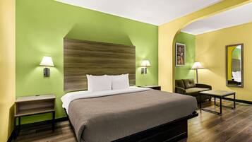 Una habitación de hotel con una cama grande, dos mesitas de noche con lámparas, un pequeño sofá y un espejo en la pared.