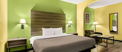 Quarto de hotel com uma cama grande, duas mesas de cabeceira com luminárias, um pequeno sofá e um espelho na parede.
