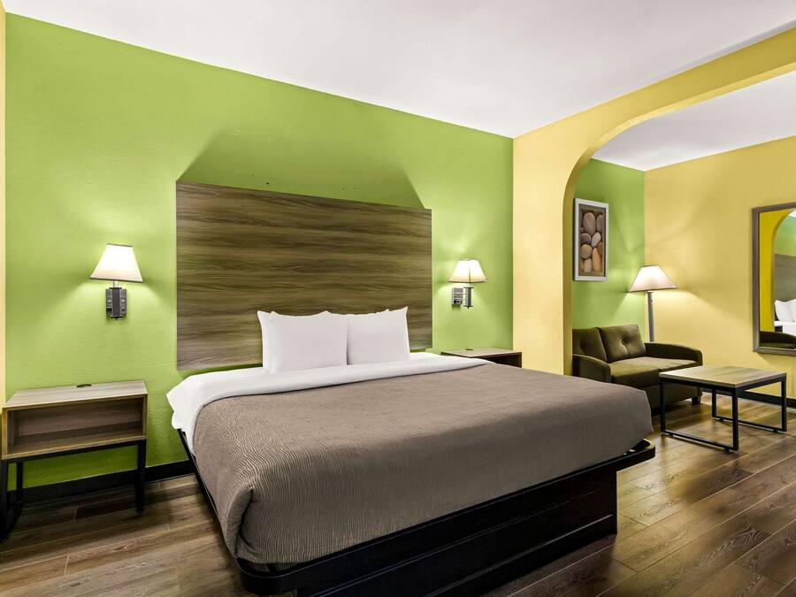 Una habitación de hotel con una cama grande, dos mesitas de noche con lámparas, un pequeño sofá y un espejo en la pared.