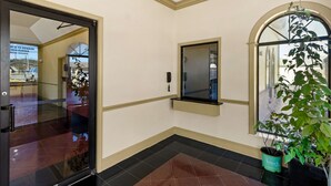 Un pasillo con una puerta de vidrio, una planta en maceta y un ventanal pequeño.