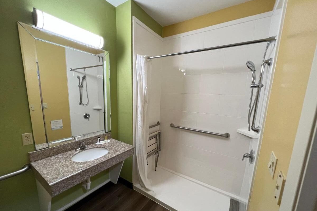A bathroom with a sink, mirror, shower, and a towel rack.
