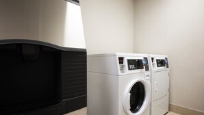 A laundry room with a front-loading washer and dryer, a black drying rack, and a tiled floor. - Holiday Inn Express & Suites DFW - Grapevine by IHG (Grapevine)