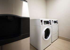 A laundry room with a front-loading washer and dryer, a black drying rack, and a tiled floor. - Holiday Inn Express & Suites DFW - Grapevine by IHG (Grapevine)