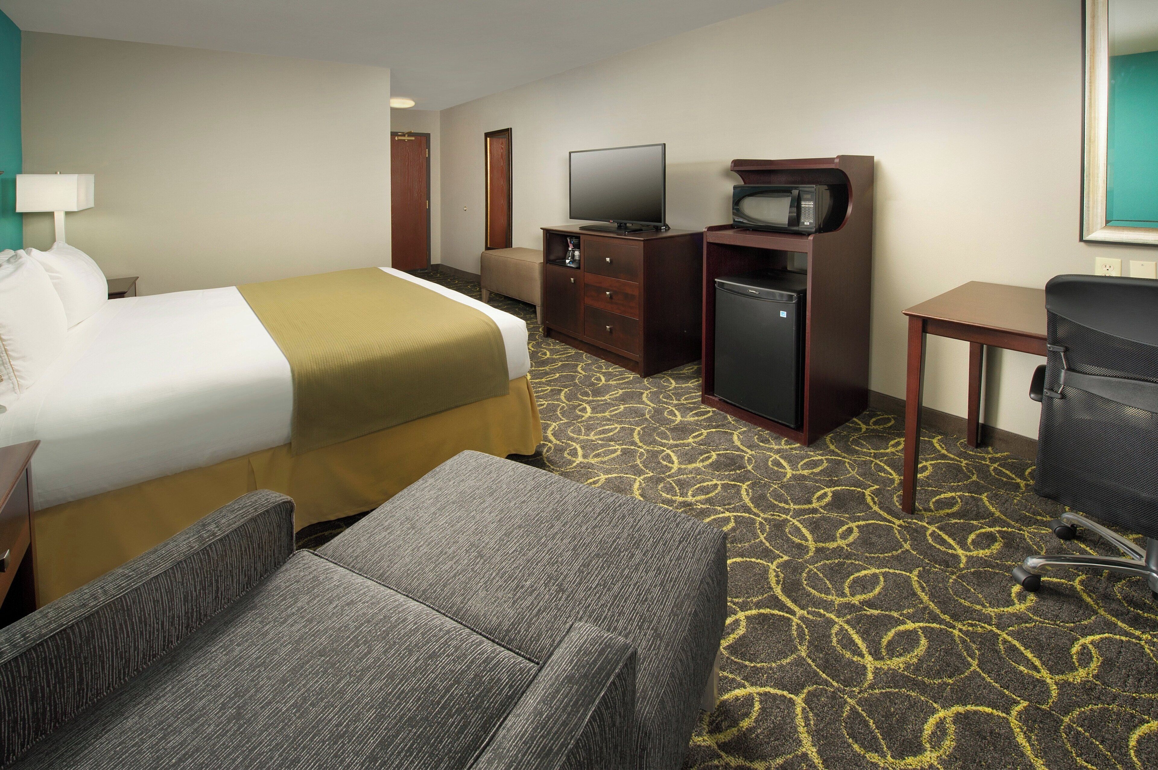 Ein Hotelzimmer mit Bett, Schreibtisch, Fernseher, Mikrowelle, Kühlschrank und einem Sessel.