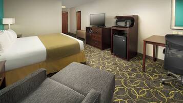 Ein Hotelzimmer mit Bett, Schreibtisch, Fernseher, Mikrowelle, Kühlschrank und einem Sessel.