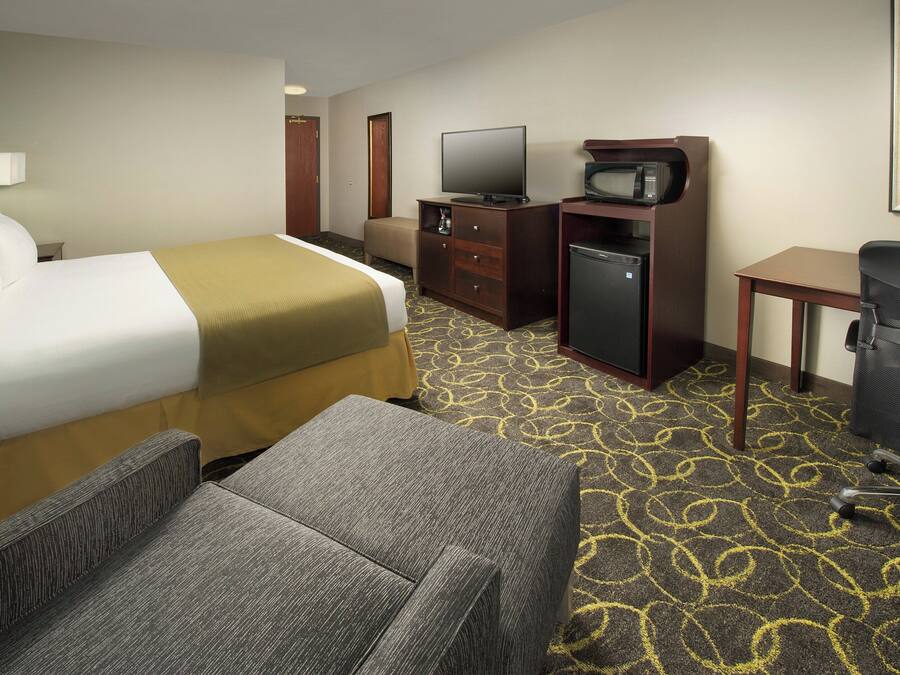 Ein Hotelzimmer mit Bett, Schreibtisch, Fernseher, Mikrowelle, Kühlschrank und einem Sessel.