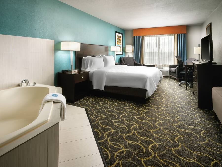 A hotel room with a bed, a desk, a TV, a bathroom with a bathtub, and a carpeted floor.
