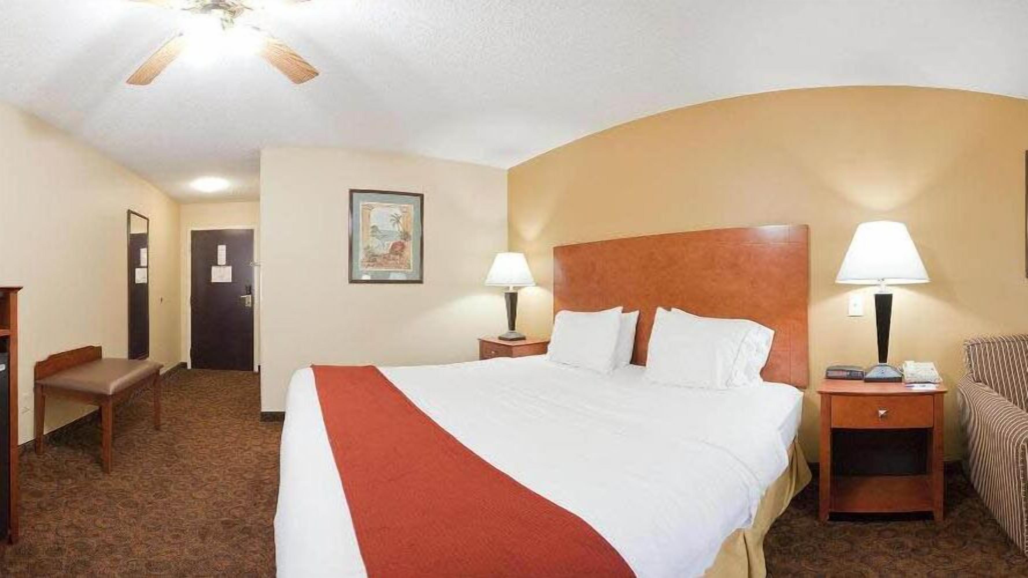 A hotel room with a large bed, two bedside tables with lamps, a desk, and a chair.