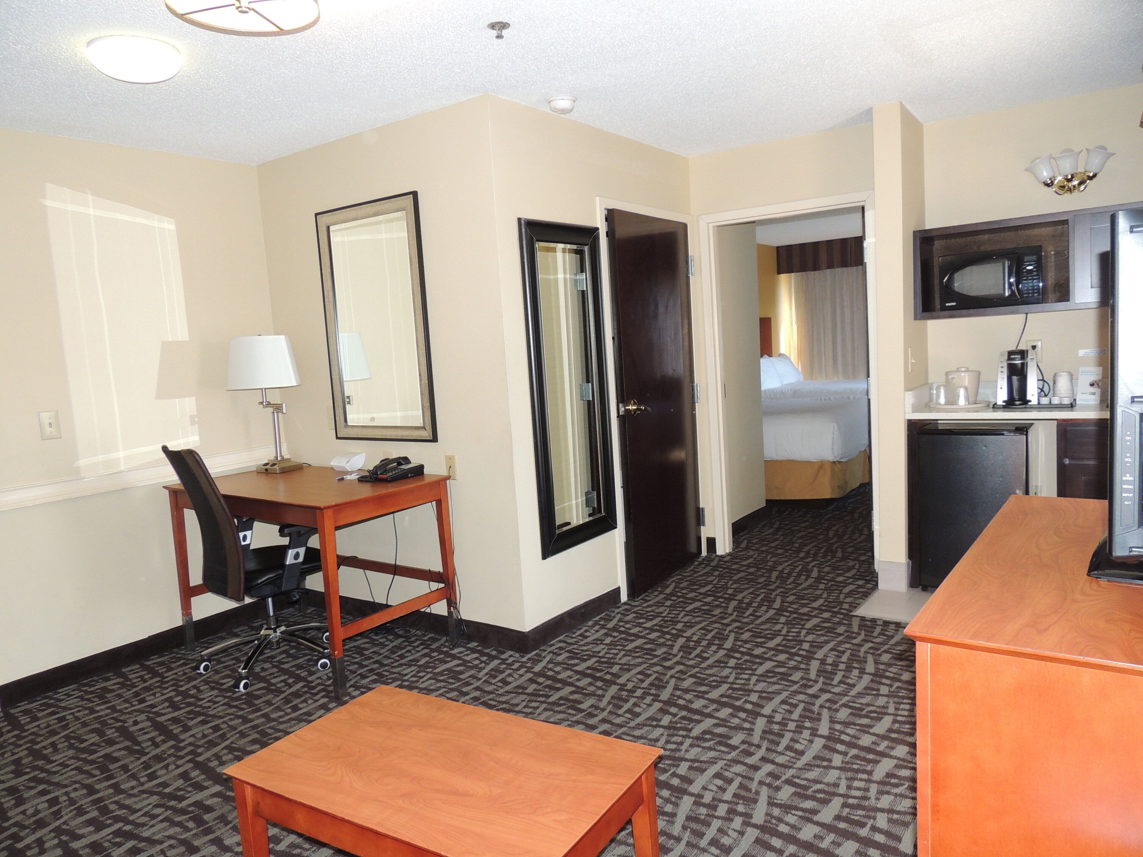 A hotel room with a desk, chair, a small table, a bed, a microwave, and a mini-fridge.