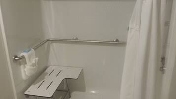 A shower area with a white shower curtain, a grab bar, a small white shelf, and a towel rack.