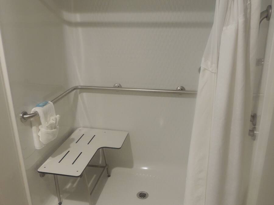 A shower area with a white shower curtain, a grab bar, a small white shelf, and a towel rack.