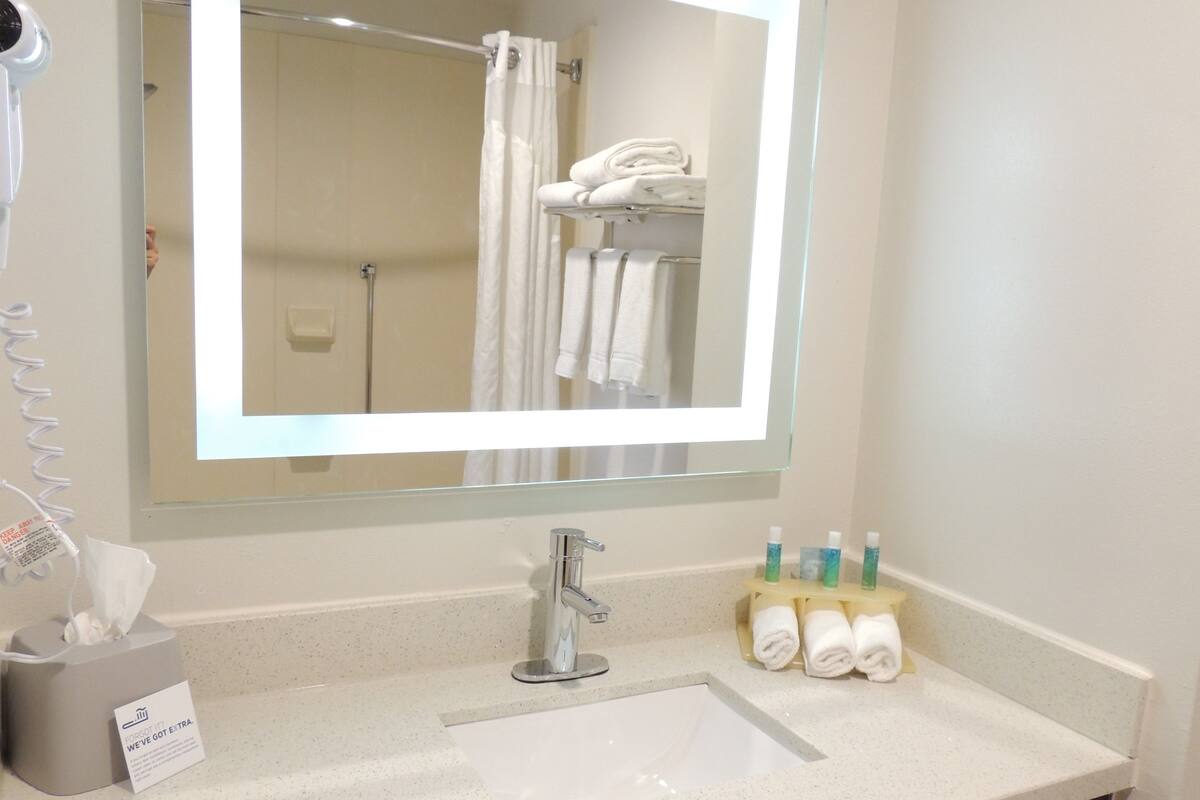 A bathroom with a sink, mirror, towel rack, and toiletries.